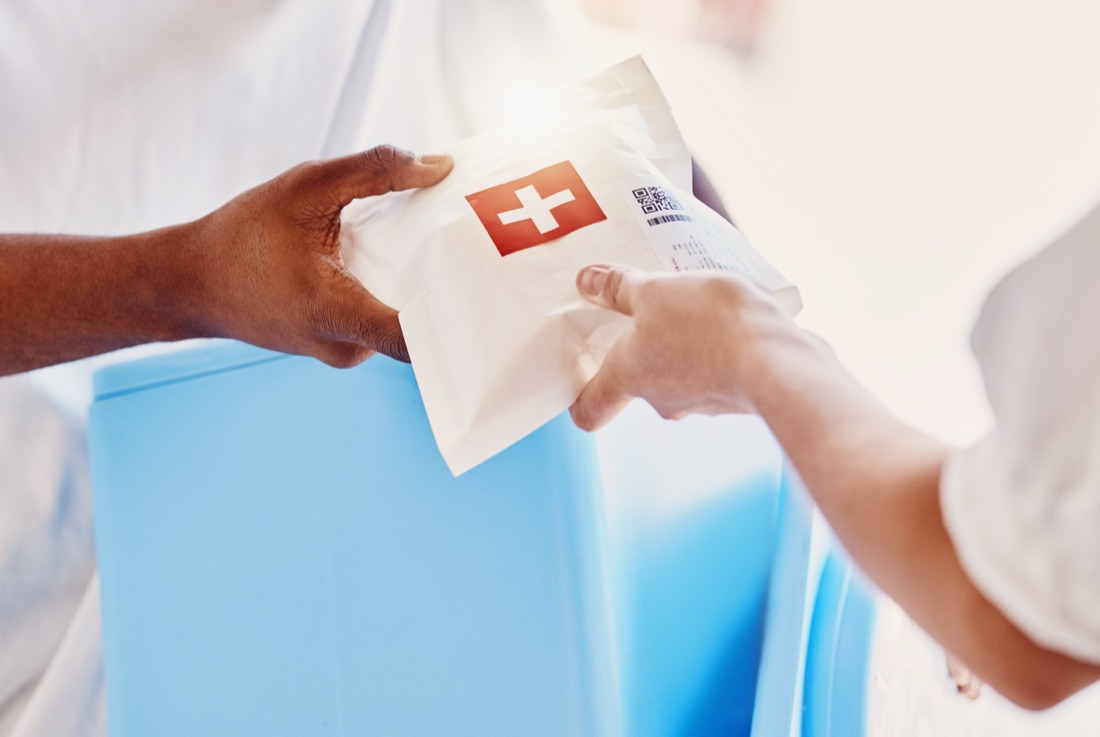 Hands exchanging a medical package marked with a red cross